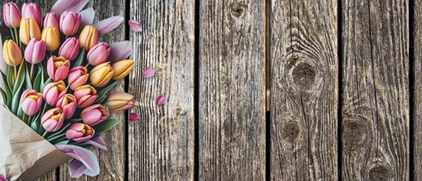 Pink and yellow tulip bouquet on rustic wooden background with soft natural lighting, horizontal floral flat lay